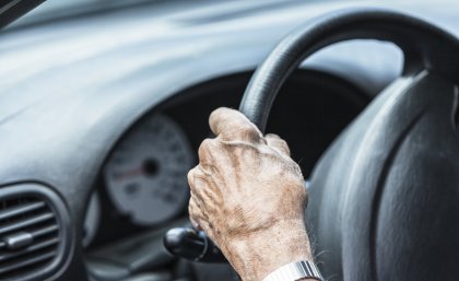 A older person with their hand on a car steering wheel.